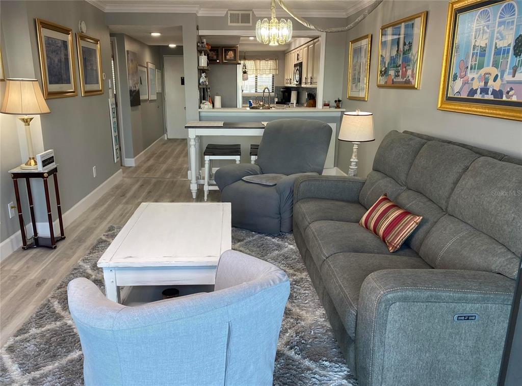 A living room features a grey sofa, armchair, coffee table, and an open kitchen area — 2465 S WASHINGTON AVENUE UNIT A202, TITUSVILLE, FL