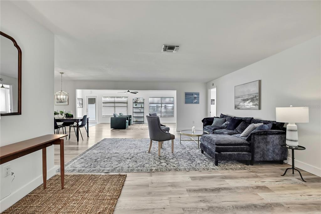 A spacious living room features light wood-look flooring, a dark sectional sofa, and neutral walls — 7231 BIG BEND DRIVE, SPRING HILL, FL