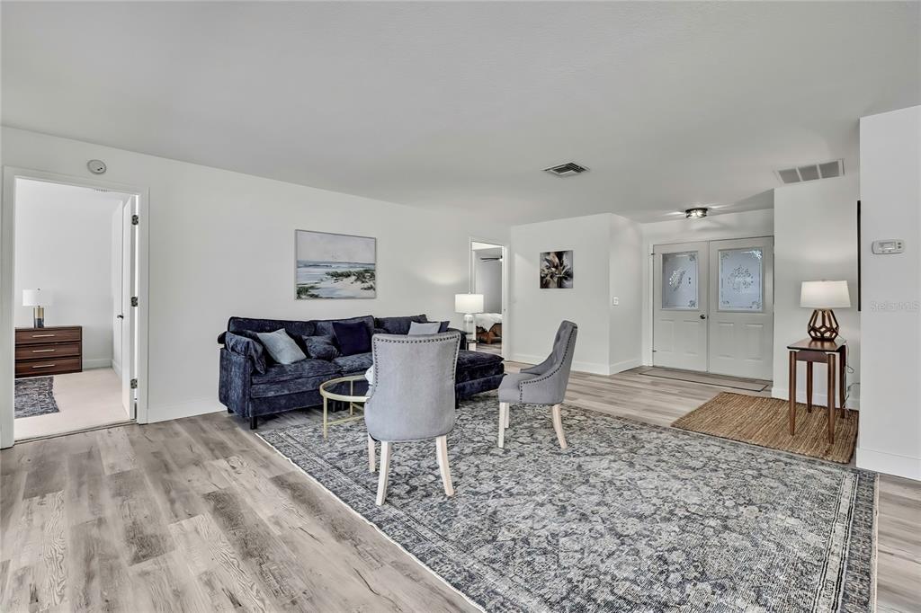 A living room features a dark blue sofa, grey chairs, and light wood-look flooring — 7231 BIG BEND DRIVE, SPRING HILL, FL