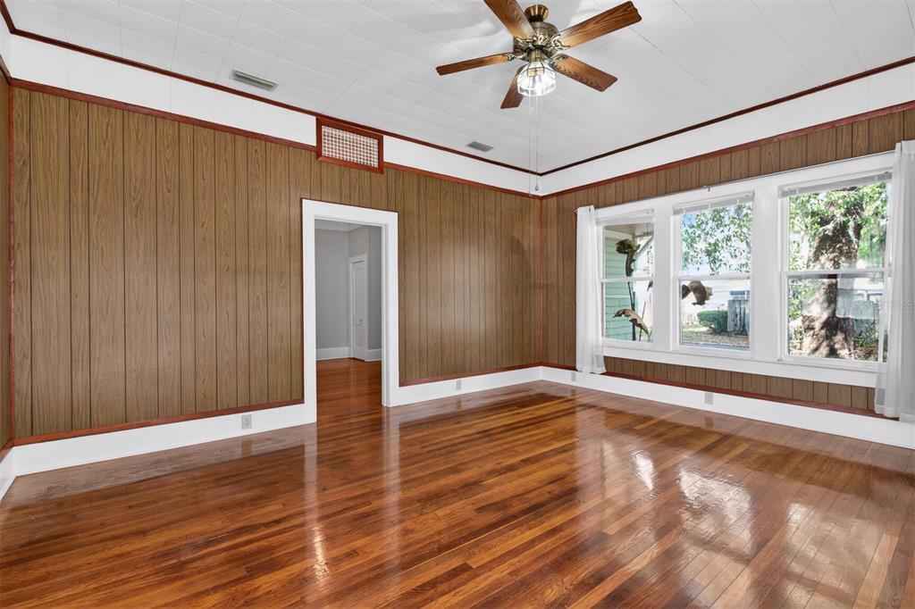An empty room features wood-paneled walls, hardwood floors, a ceiling fan, and three windows — 630 NE 6TH AVENUE, GAINESVILLE, FL