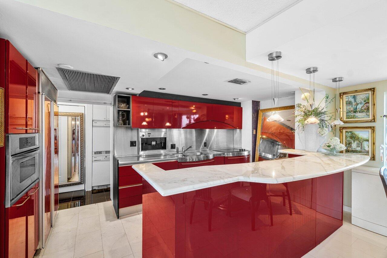 A kitchen features red high-gloss cabinets, a marble breakfast bar, and stainless steel appliances — 2774 S Ocean Boulevard # 708, Palm Beach FL 33480, PALM BEACH, FL