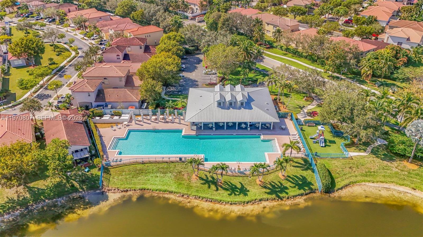 An aerial view shows a community swimming pool, clubhouse, and playground next to a lake — 3736 NE 9 CT, Homestead FL 33033, HOMESTEAD, FL