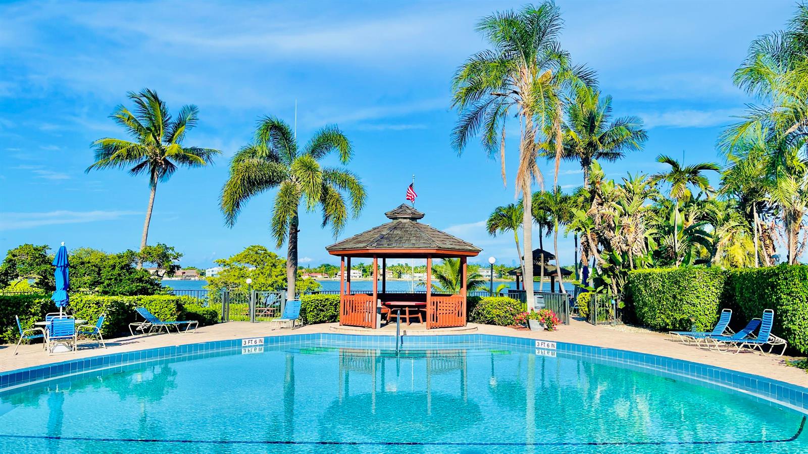 A swimming pool with a gazebo sits in front of palm trees and a blue sky — 7030 Half Moon Circle # 121, Hypoluxo FL 33462, HYPOLUXO, FL