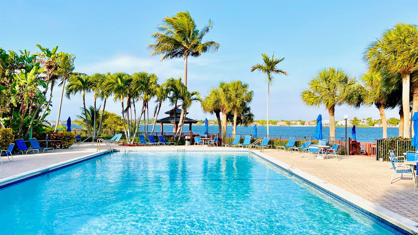 A swimming pool with lounge chairs and palm trees overlooking a bay — 7030 Half Moon Circle # 121, Hypoluxo FL 33462, HYPOLUXO, FL
