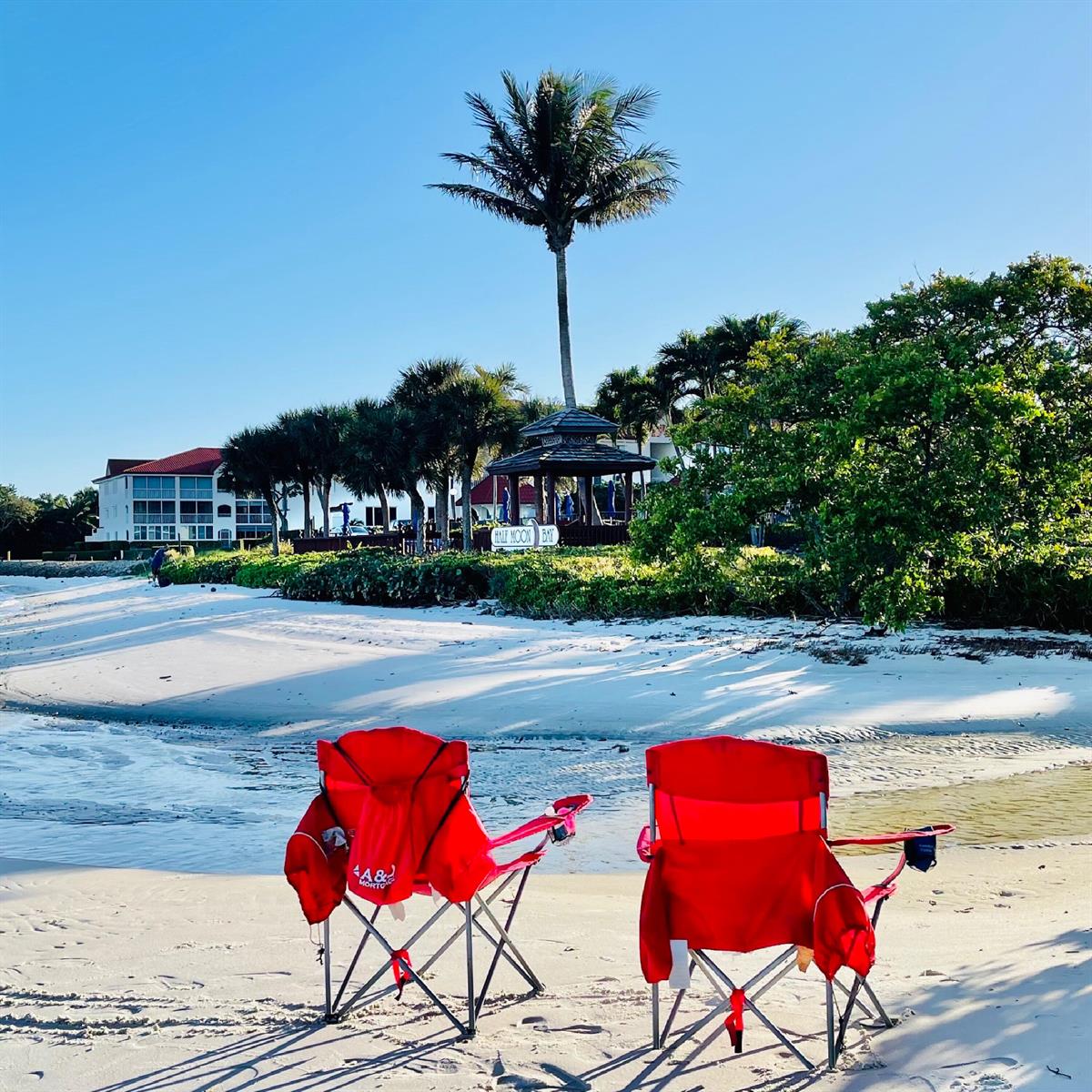 Two red folding chairs sit on a sandy beach facing a gazebo and palm trees — 7030 Half Moon Circle # 121, Hypoluxo FL 33462, HYPOLUXO, FL