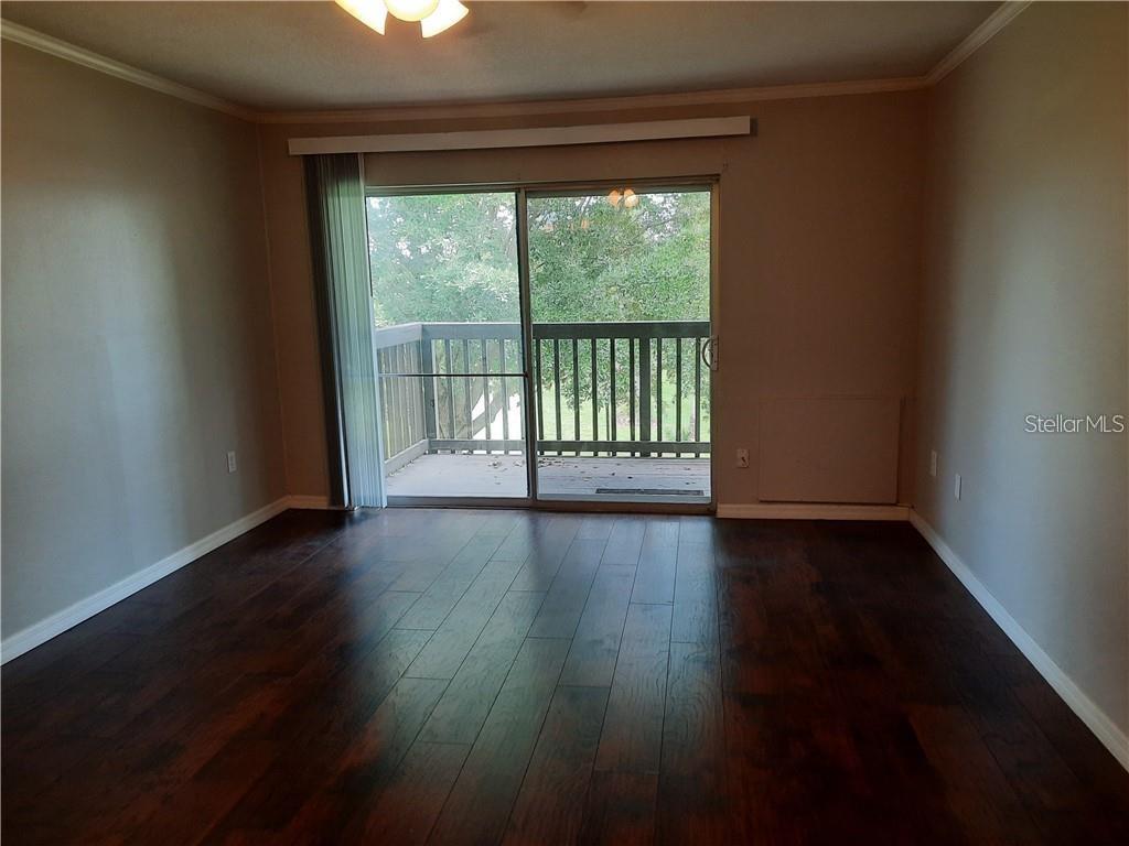 A living room features dark wood-look flooring, beige walls, and a sliding glass balcony door — 1695 LEE ROAD UNIT B210, WINTER PARK, FL
