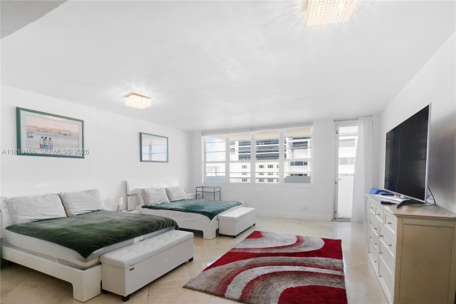 A bedroom features two beds, a red patterned rug, and a television on a dresser — 100 Lincoln Rd # 827, Miami Beach FL 33139, MIAMI BEACH, FL