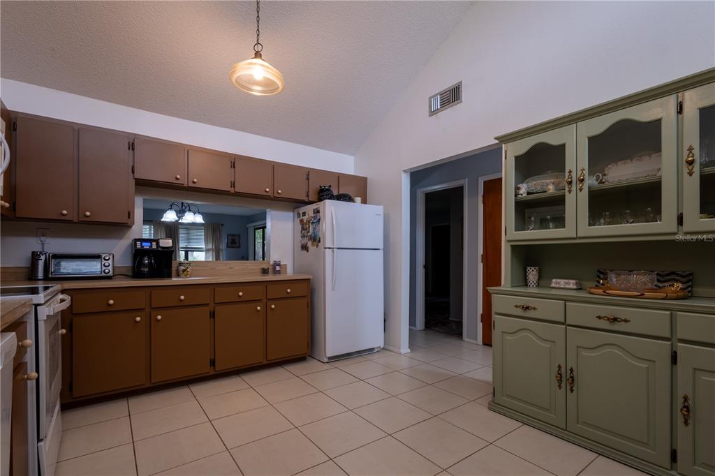 A kitchen features brown cabinets, a white refrigerator, and a green hutch on tile flooring — 7913 PINEGLEN COURT UNIT 34, SARASOTA, FL
