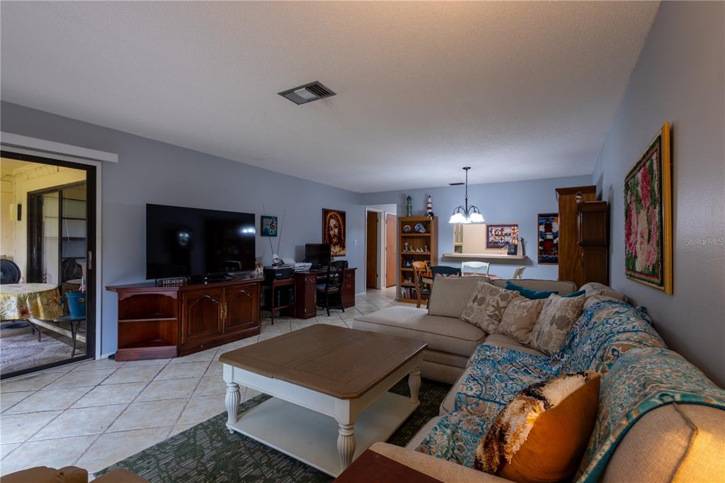 A living room features tile flooring, a sectional sofa, a television console, and a dining area — 7913 PINEGLEN COURT UNIT 34, SARASOTA, FL
