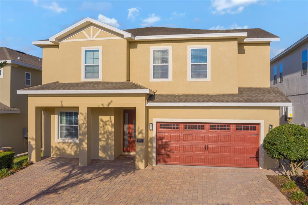 A two-story house with a tan stucco exterior, a red garage door, and a paved driveway — 7643 WILMINGTON LOOP, KISSIMMEE, FL