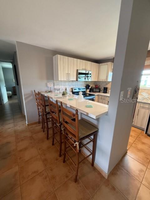 A kitchen with light wood cabinets, a white breakfast bar, and three wooden bar stools — Cond. Bosque del Mar EDIFICIO A UNIT H-302, RIO GRANDE, PR