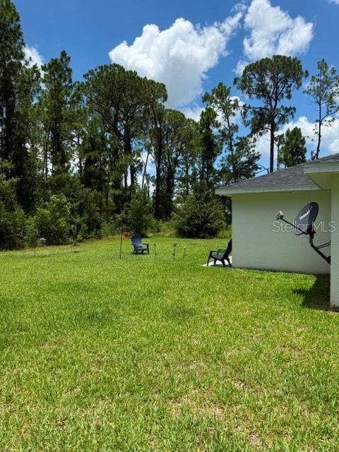 A grassy backyard features a house corner with a satellite dish and outdoor chairs — 5421 PONCE DE LEON BOULEVARD, SEBRING, FL