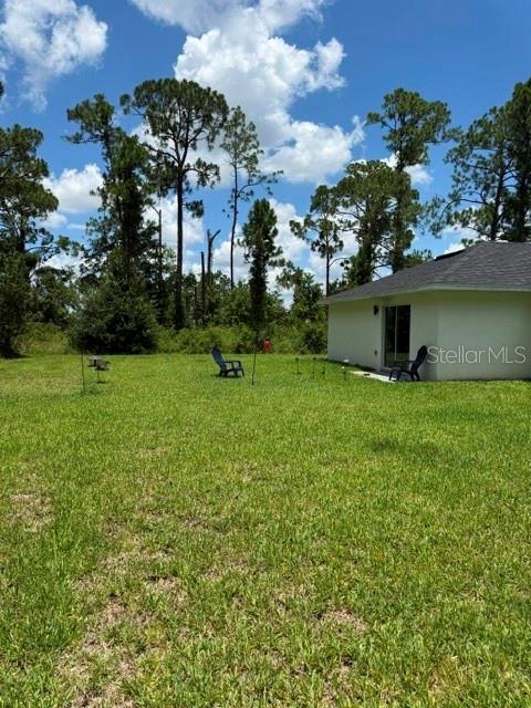 A grassy backyard features a house corner and two blue chairs near a wooded area — 5421 PONCE DE LEON BOULEVARD, SEBRING, FL