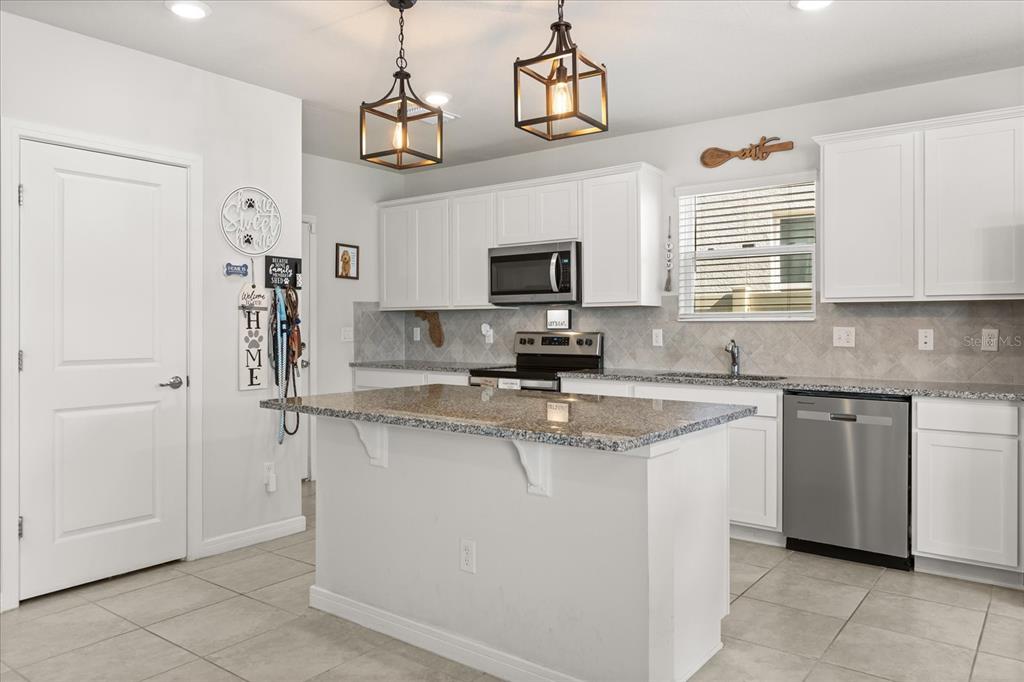A kitchen features white cabinets, granite countertops, a central island, and stainless steel appliances — 2224 CANOPY TERRACE BOULEVARD, DELAND, FL