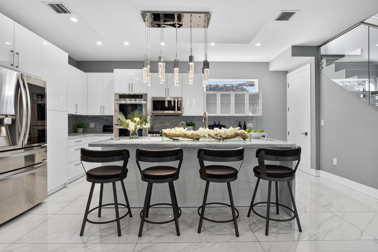 A modern kitchen features white cabinetry, a marble-topped island, four bar stools, and pendant lighting — 69 S Cortez Drive # 69, Margate FL 33068, MARGATE, FL