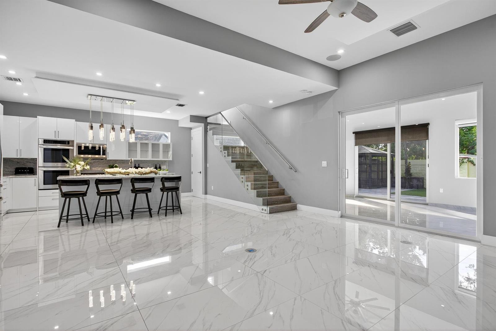 A modern kitchen with white cabinetry and a marble island sits beside a glass-railed staircase — 69 S Cortez Drive # 69, Margate FL 33068, MARGATE, FL