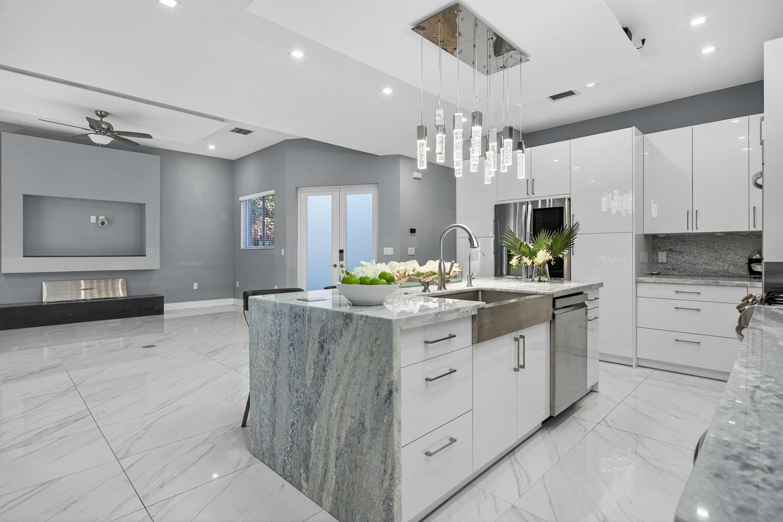 A modern kitchen features a large stone island, white cabinetry, and gray tile flooring — 69 S Cortez Drive # 69, Margate FL 33068, MARGATE, FL