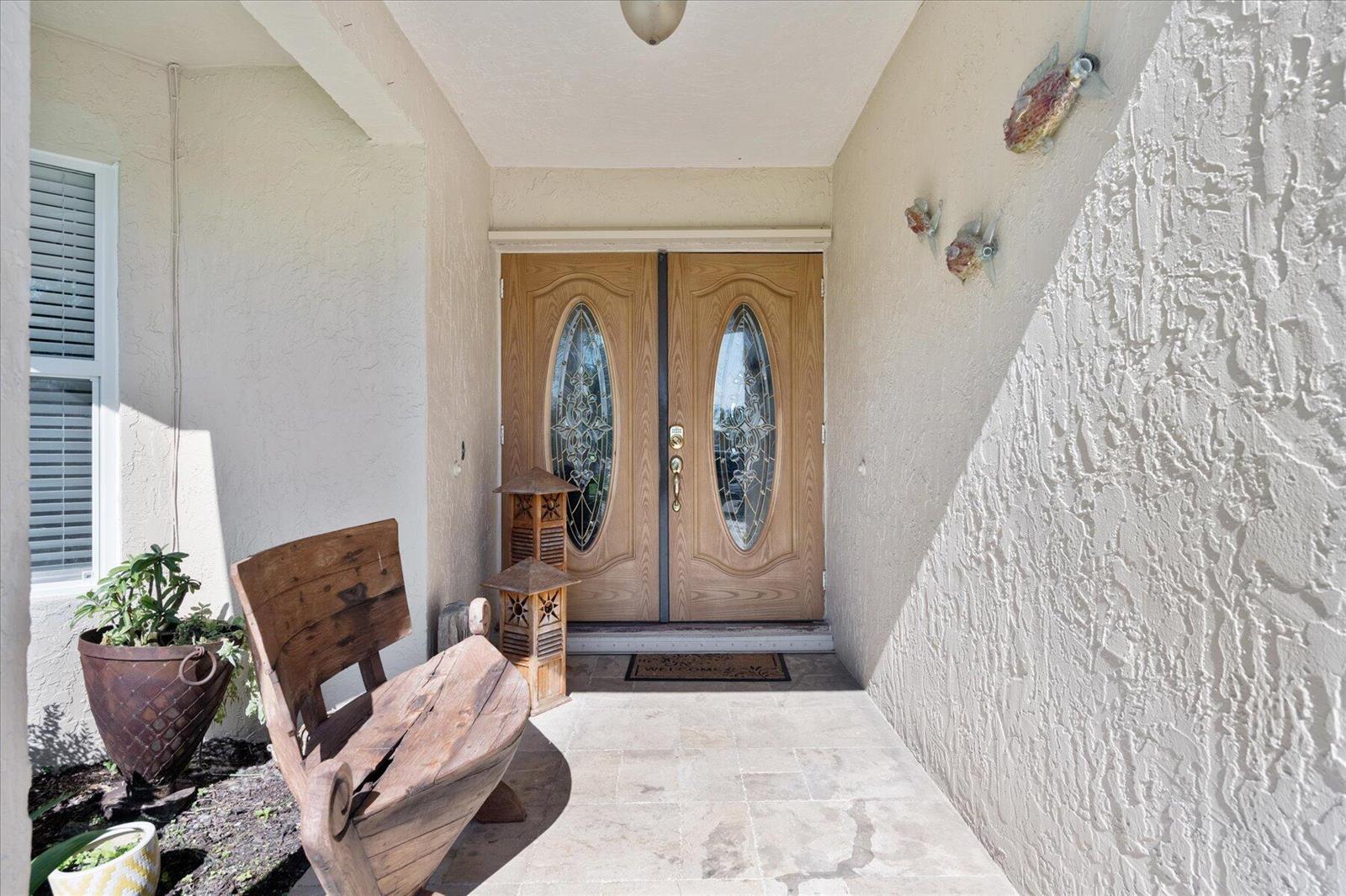 A covered entryway features double wooden doors with glass inserts, a stone floor, and a bench — 13889 Geranium Place, Wellington FL 33414, WELLINGTON, FL