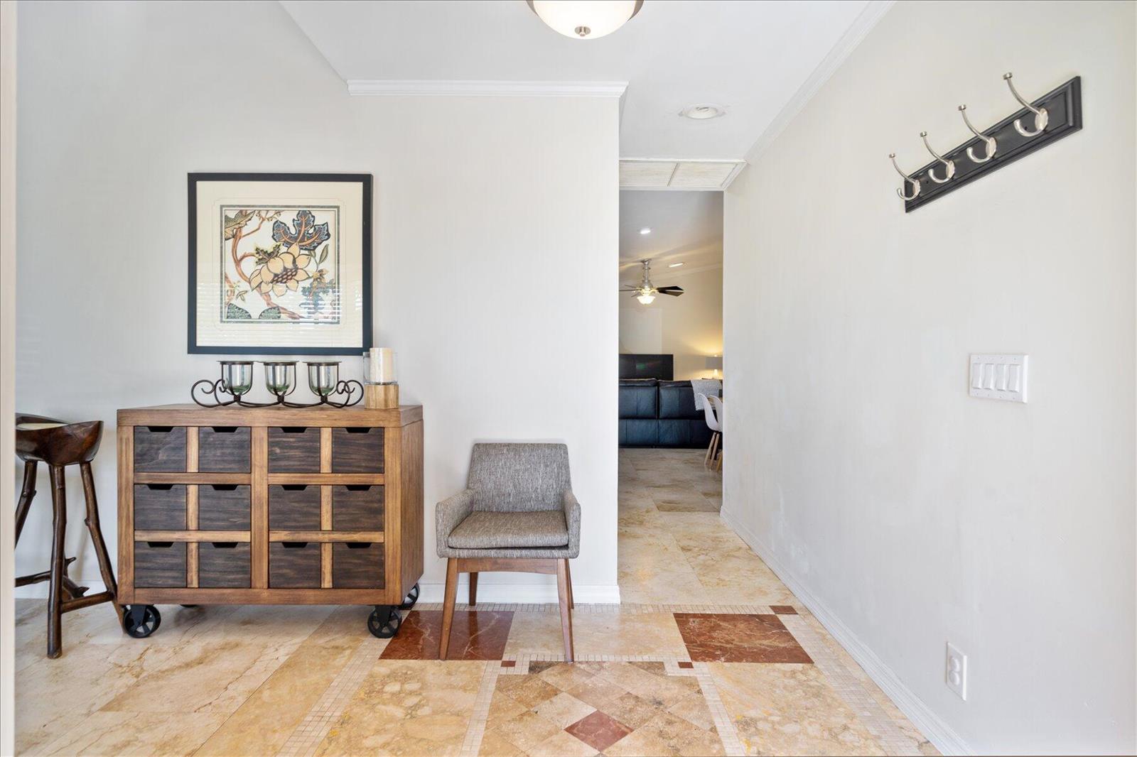 An entryway features a wooden cabinet, a gray chair, and a wall-mounted coat rack — 13889 Geranium Place, Wellington FL 33414, WELLINGTON, FL