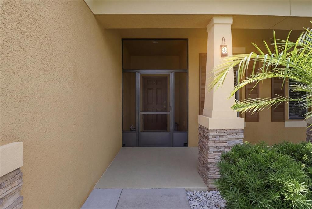 A covered entryway features a screen door, stone pillar base, and tan stucco walls — 2109 TRILLIUM BOULEVARD, BROOKSVILLE, FL