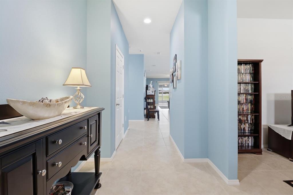 A hallway with light blue walls, tile flooring, a black console table, and a bookshelf — 2109 TRILLIUM BOULEVARD, BROOKSVILLE, FL
