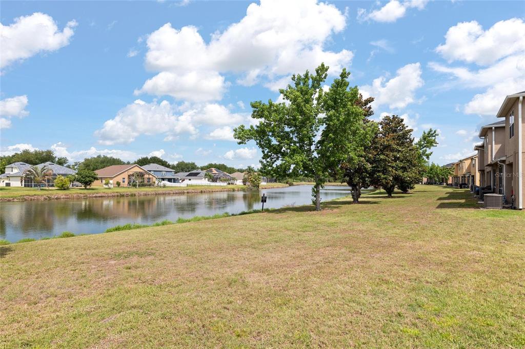 A grassy lawn overlooks a pond with residential houses and trees in the background — 6981 TOWERING SPRUCE DRIVE, RIVERVIEW, FL