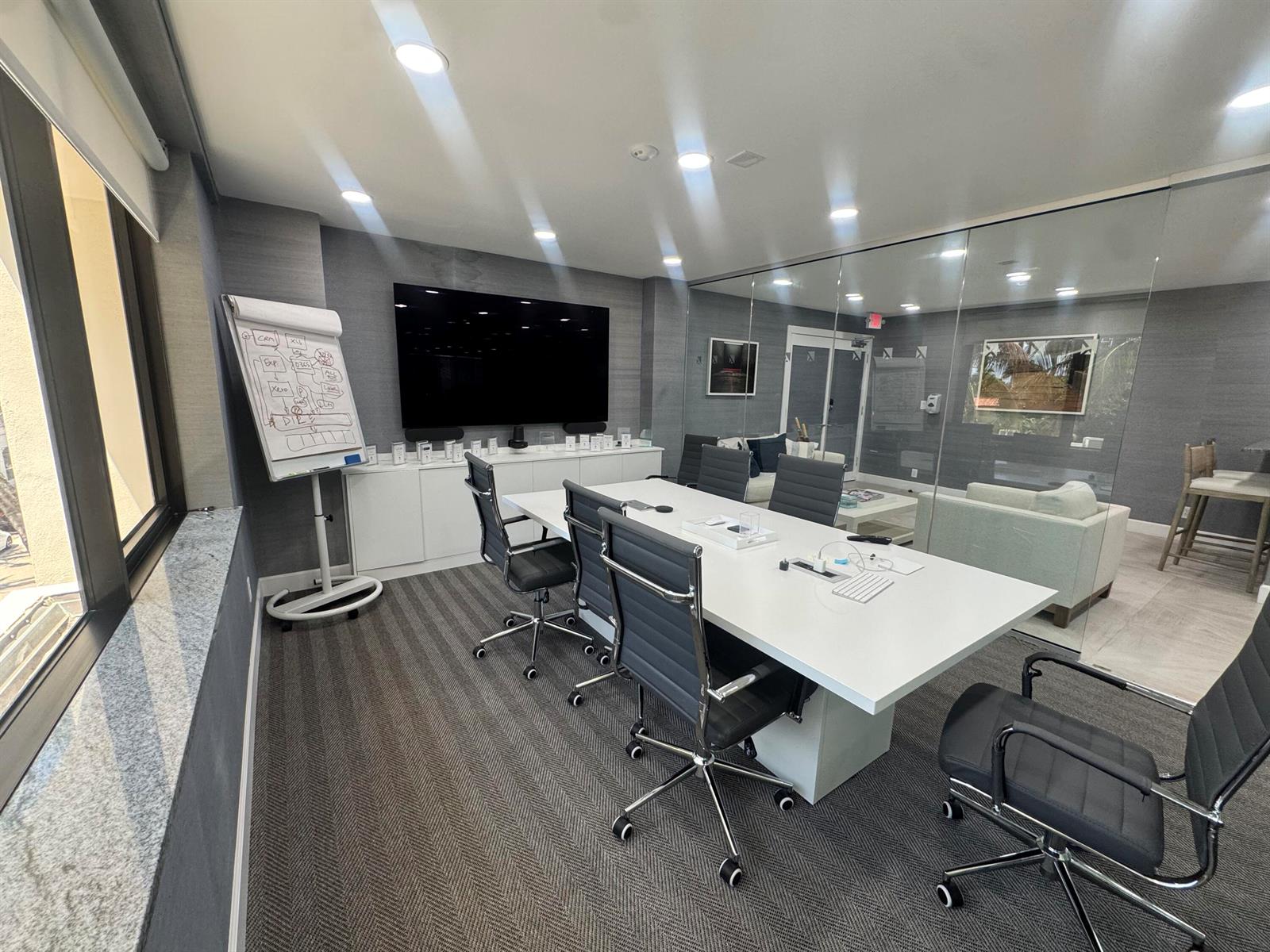 A modern conference room features a long white table, rolling chairs, and a wall-mounted television — 201 Worth Avenue # 301, Palm Beach FL 33480, PALM BEACH, FL