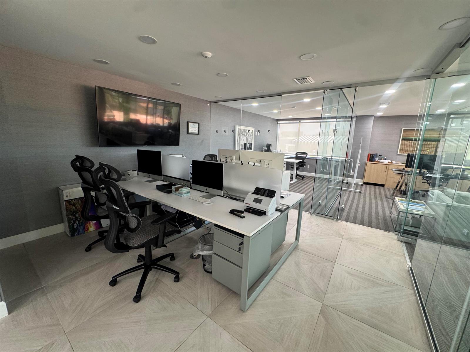 A modern office space features a shared desk, glass partitions, and gray-toned interior finishes — 201 Worth Avenue # 301, Palm Beach FL 33480, PALM BEACH, FL