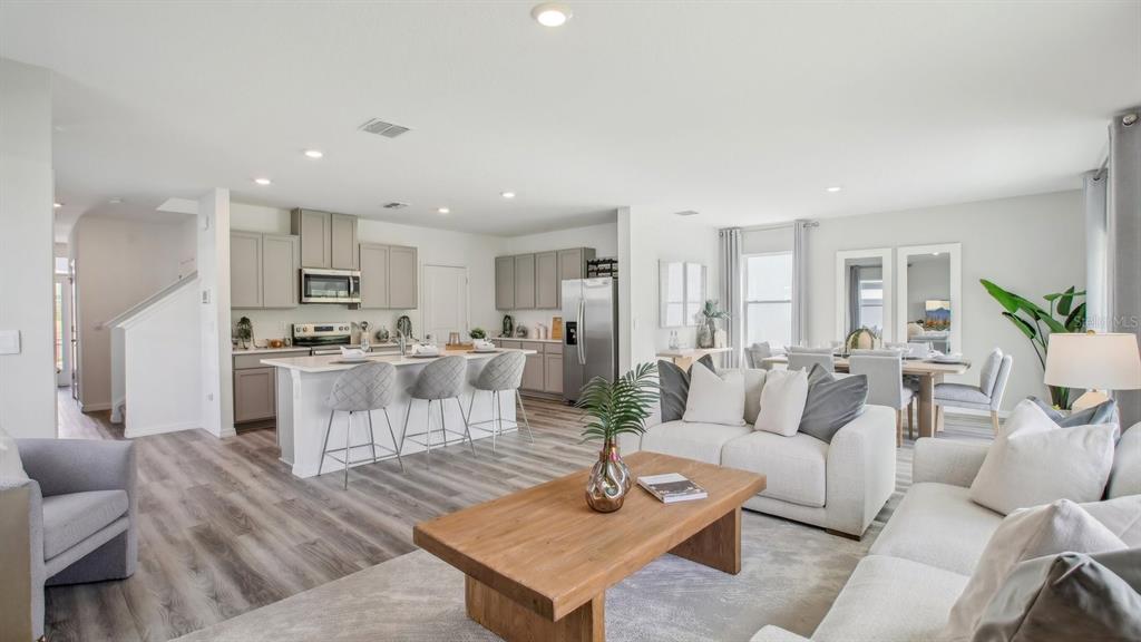 An open-concept living room and kitchen featuring light wood flooring and neutral-toned furniture — 8312 RIVERBEND RISE LANE, TAMPA, FL