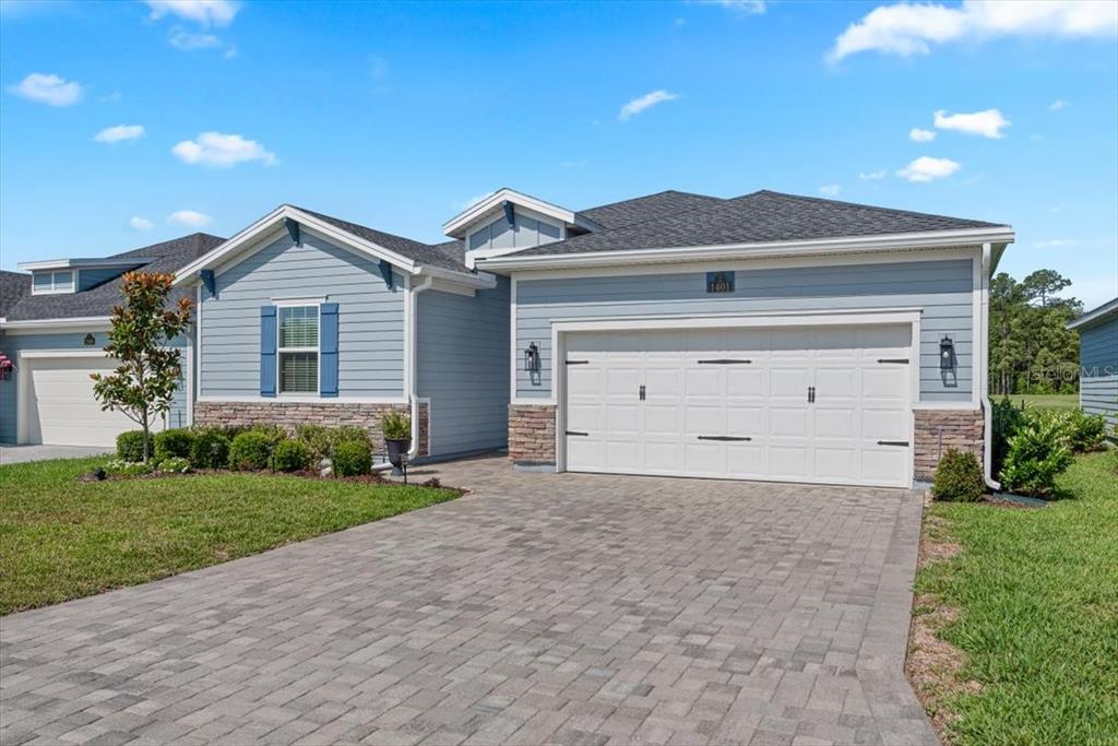 A light blue house with a stone base, white garage door, and paver driveway — 1401 STILLWATER BOULEVARD, ST JOHNS, FL