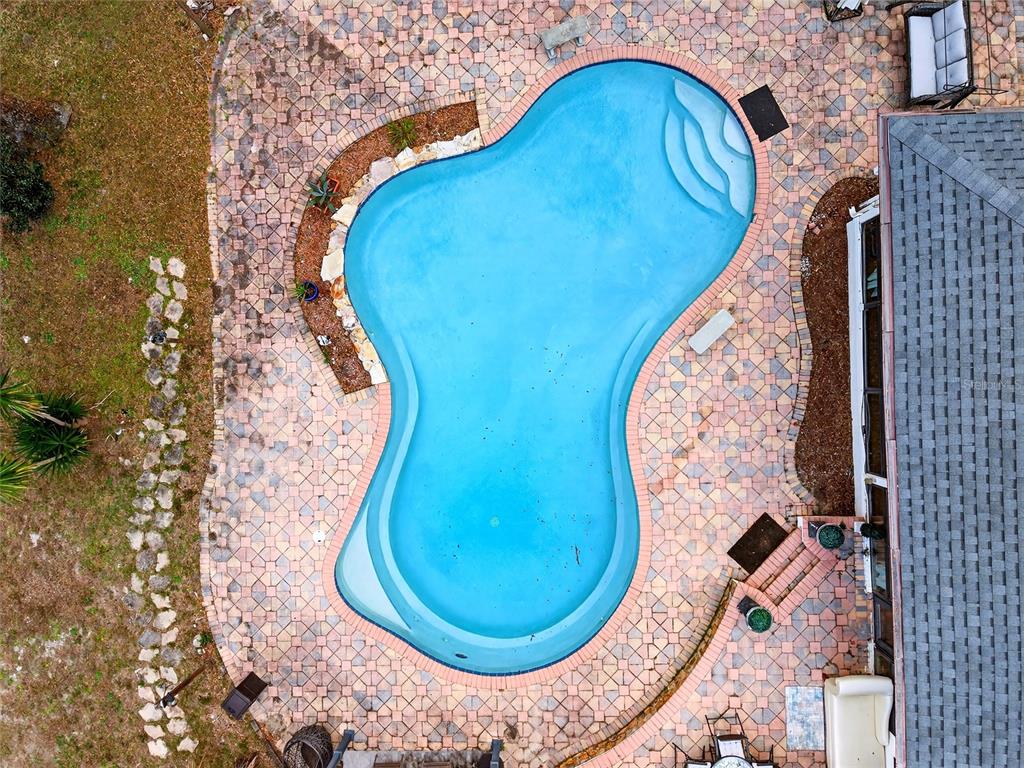 An aerial view shows a freeform swimming pool surrounded by a paved patio and landscaping — 11795 SW HIGHWAY 484, DUNNELLON, FL