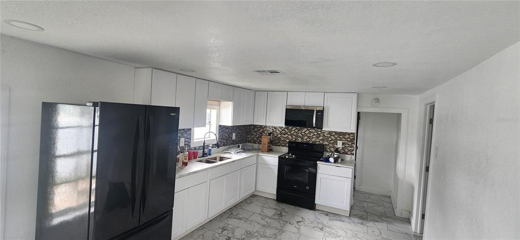 A kitchen features white cabinets, black appliances, a mosaic tile backsplash, and marble-patterned tile flooring — 3004 E DR MARTIN LUTHER KING JR BOULEVARD, TAMPA, FL