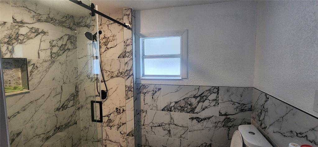 A bathroom features a glass-enclosed shower with marble-patterned tile and a matching tiled wall — 3004 E DR MARTIN LUTHER KING JR BOULEVARD, TAMPA, FL