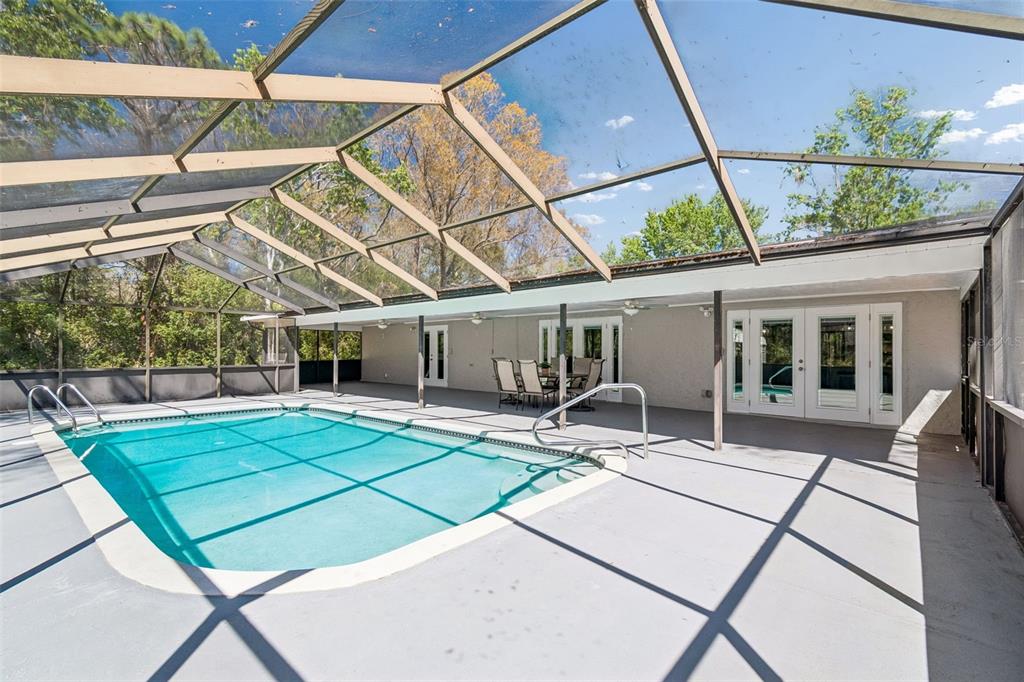 A swimming pool with a screen enclosure on a concrete patio next to a house — 10909 CANDY LANE, NEW PORT RICHEY, FL