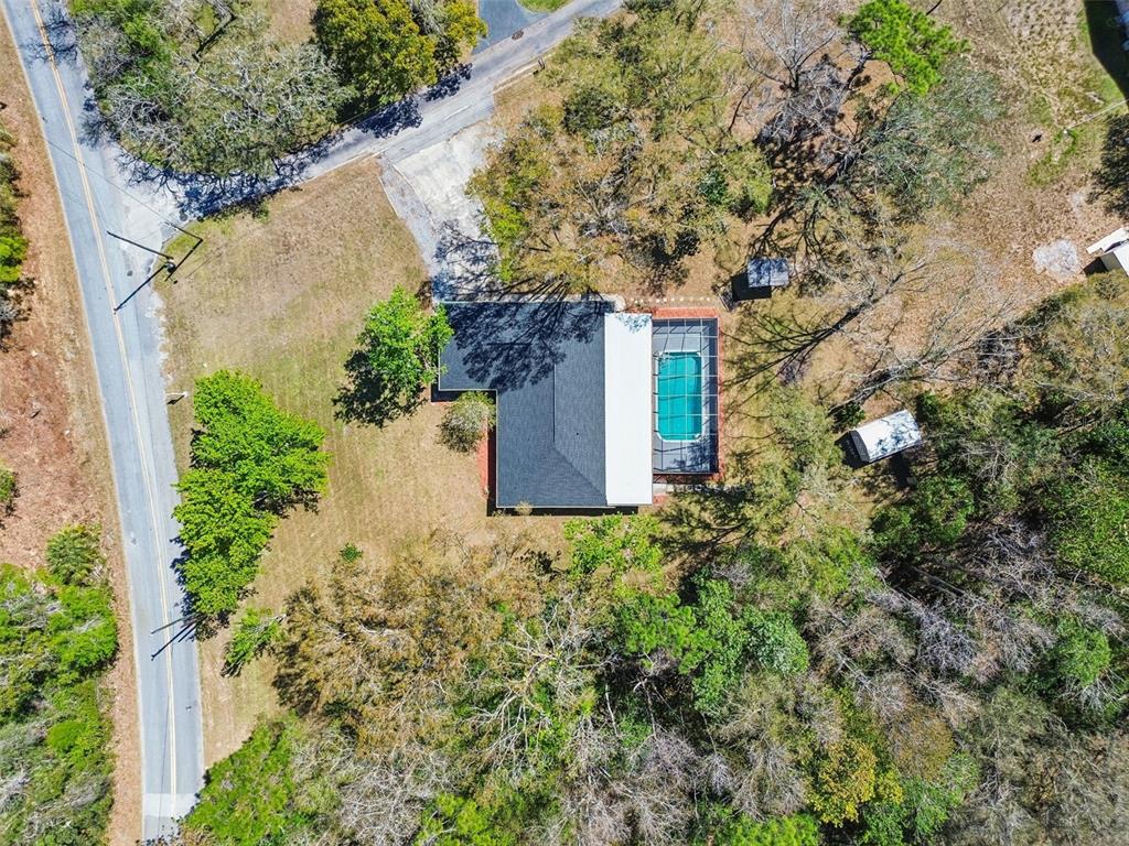 An aerial view shows a house with a pool enclosure surrounded by trees and roads — 10909 CANDY LANE, NEW PORT RICHEY, FL