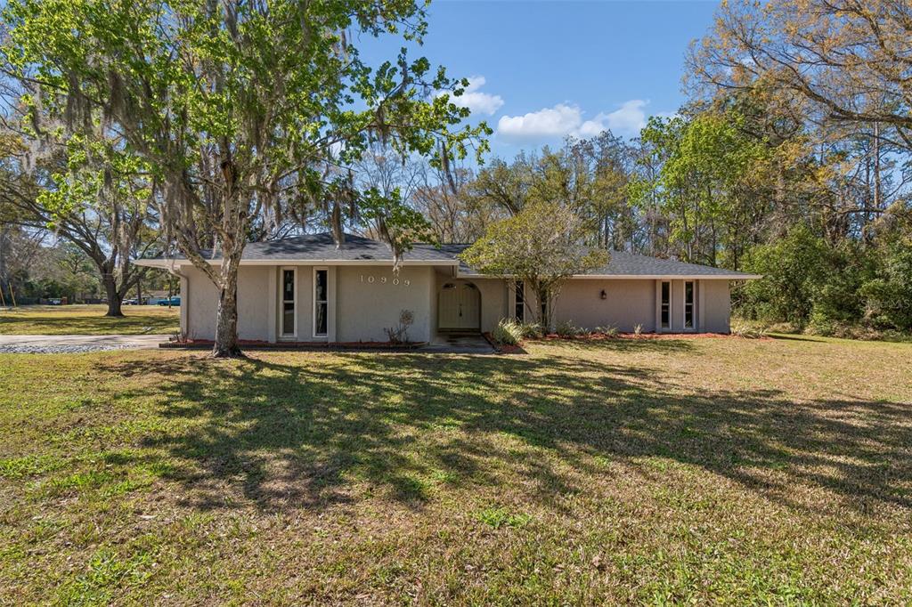 A single-story house with a beige exterior and a dark roof sits on a lawn — 10909 CANDY LANE, NEW PORT RICHEY, FL