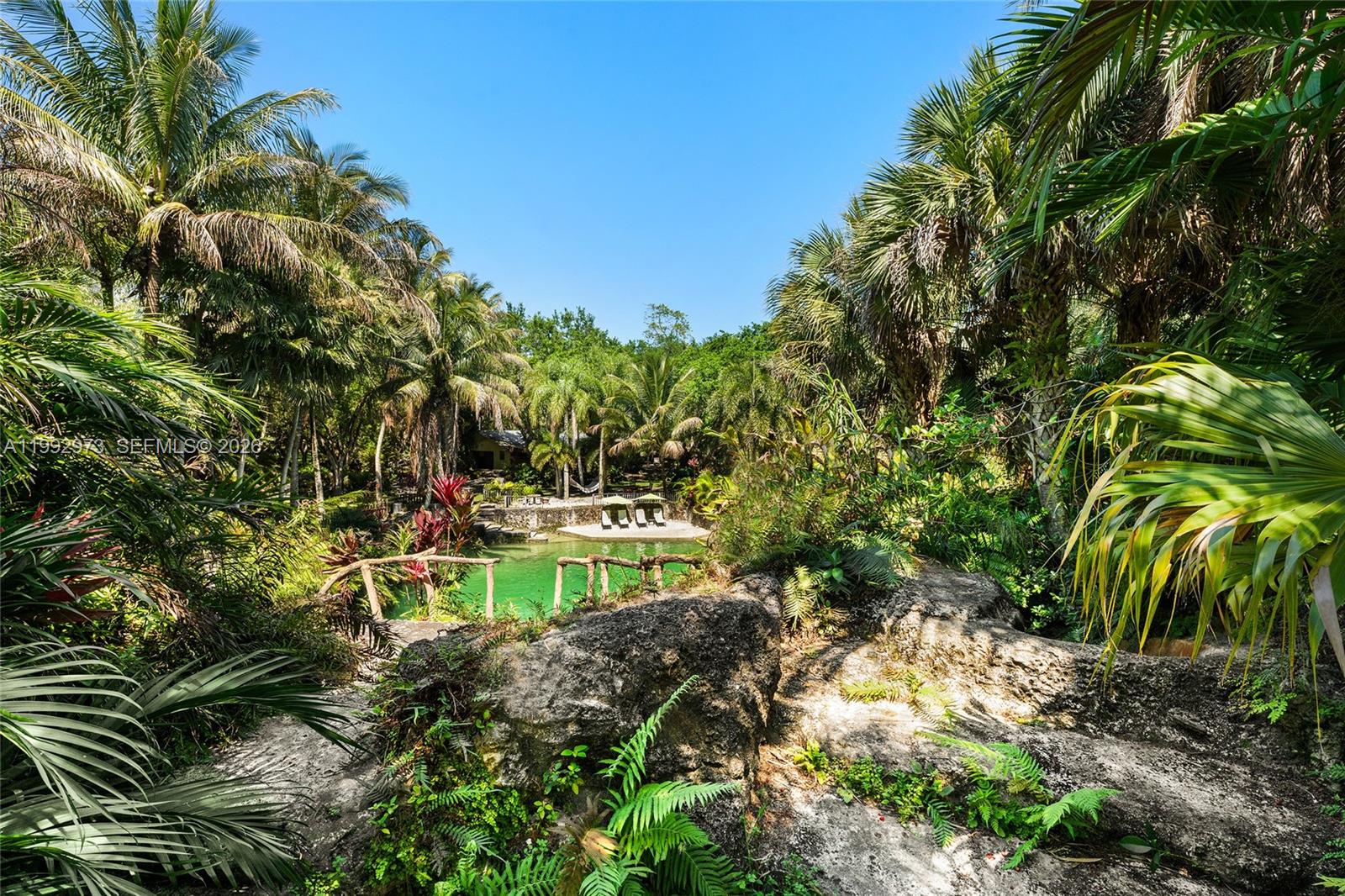 A lush, tropical backyard features a natural rock formation overlooking a green swimming pool — 15000 SW 200th St, Miami FL 33187, MIAMI, FL