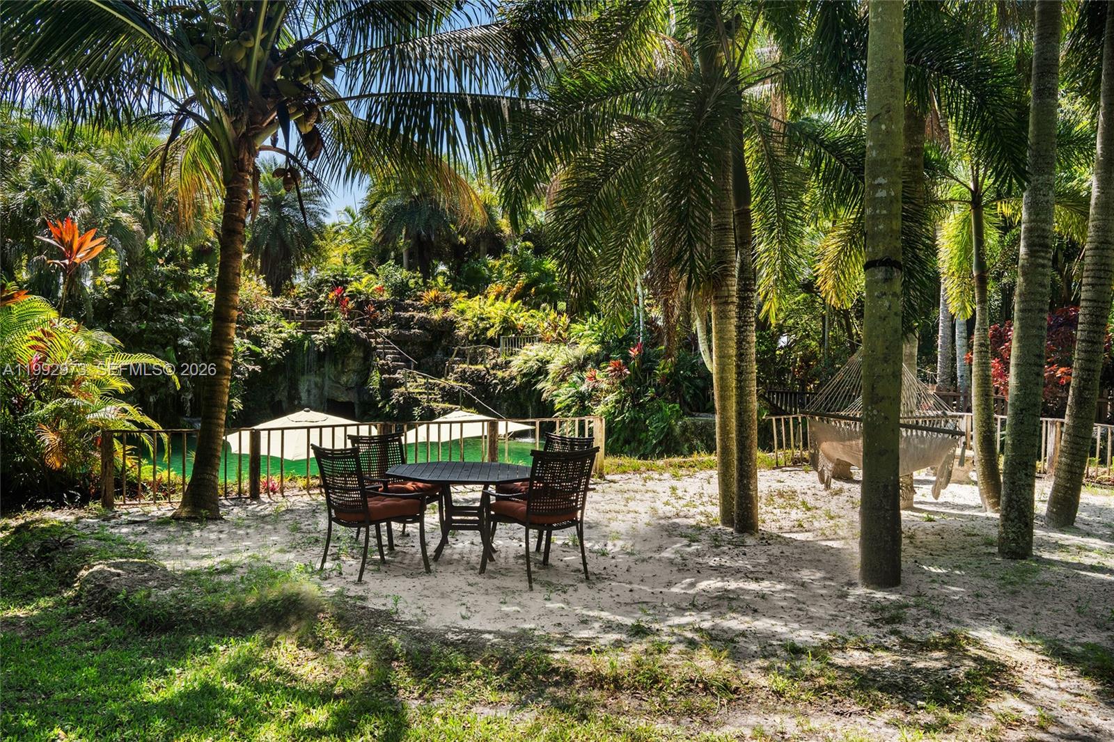 A patio with a dining set and hammock sits on a sandy area near water — 15000 SW 200th St, Miami FL 33187, MIAMI, FL