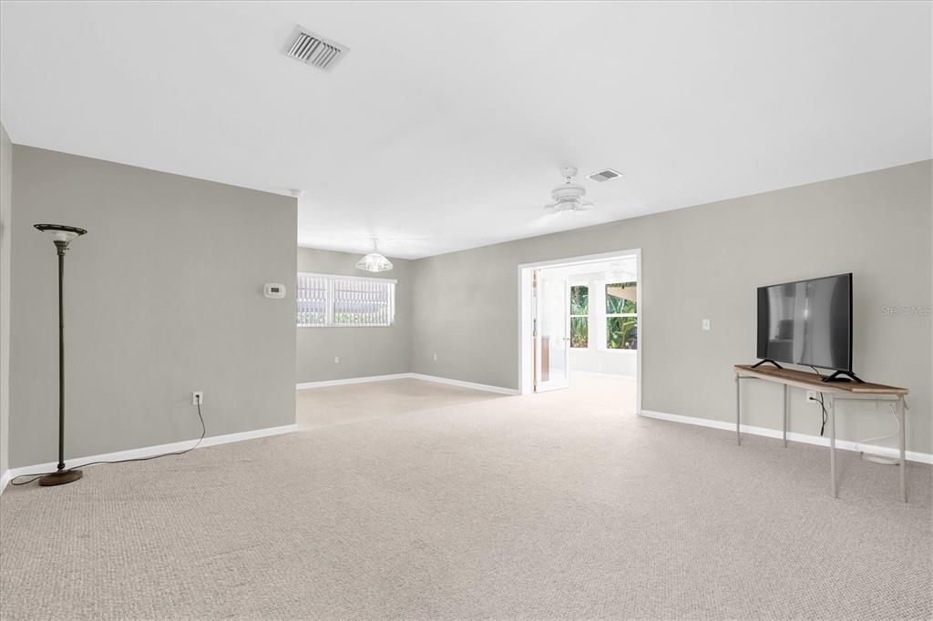 A spacious living room features neutral walls, beige carpeting, a television on a console table — 1936 NUGGET DRIVE, CLEARWATER, FL