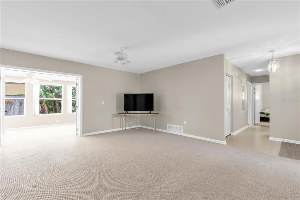 A carpeted living room features a television on a table and a doorway to a sunroom — 1936 NUGGET DRIVE, CLEARWATER, FL