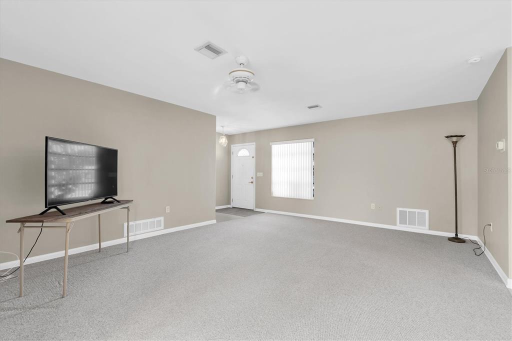A living room with beige walls, gray carpeting, a ceiling fan, and a television on a stand — 1936 NUGGET DRIVE, CLEARWATER, FL