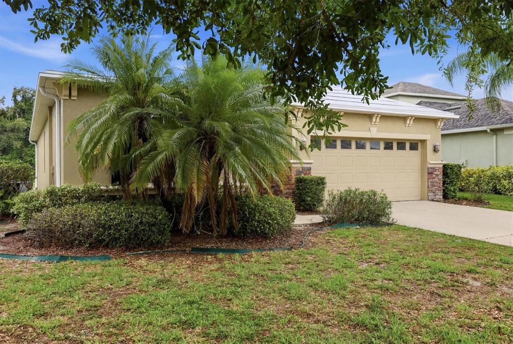 A tan house with a two-car garage, stone accents, and a large palm tree — 12218 LAVENDER LOOP, BRADENTON, FL