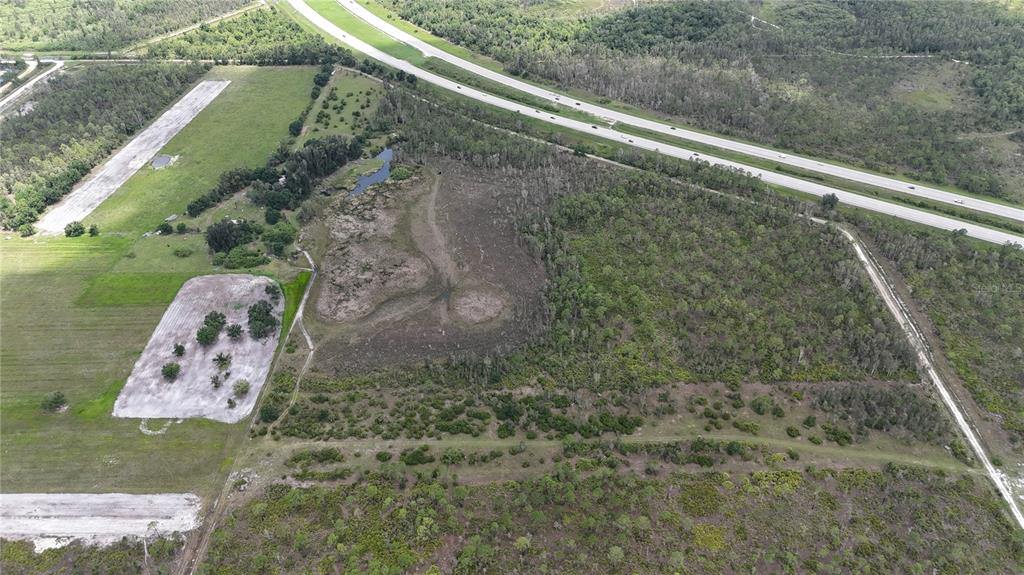 An aerial view shows a large plot of land with a pond, trees, and a highway — 21061 GRANVILLE ROAD, NORTH FORT MYERS, FL
