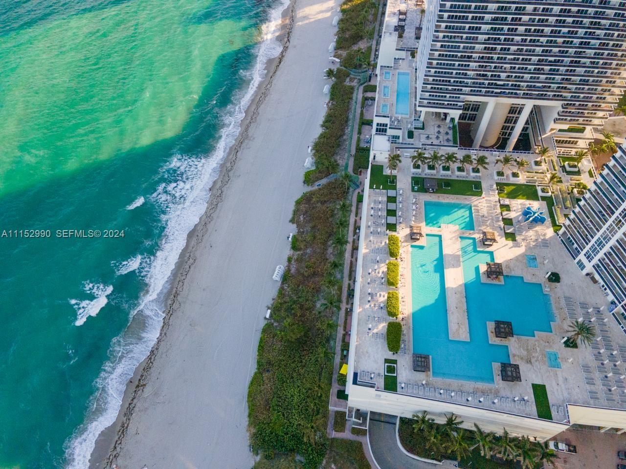 An aerial view shows a beachfront resort with multiple swimming pools and a tall building — 1830 OCEAN DR # 4710, Hallandale Beach FL 33009, HALLANDALE BEACH, FL