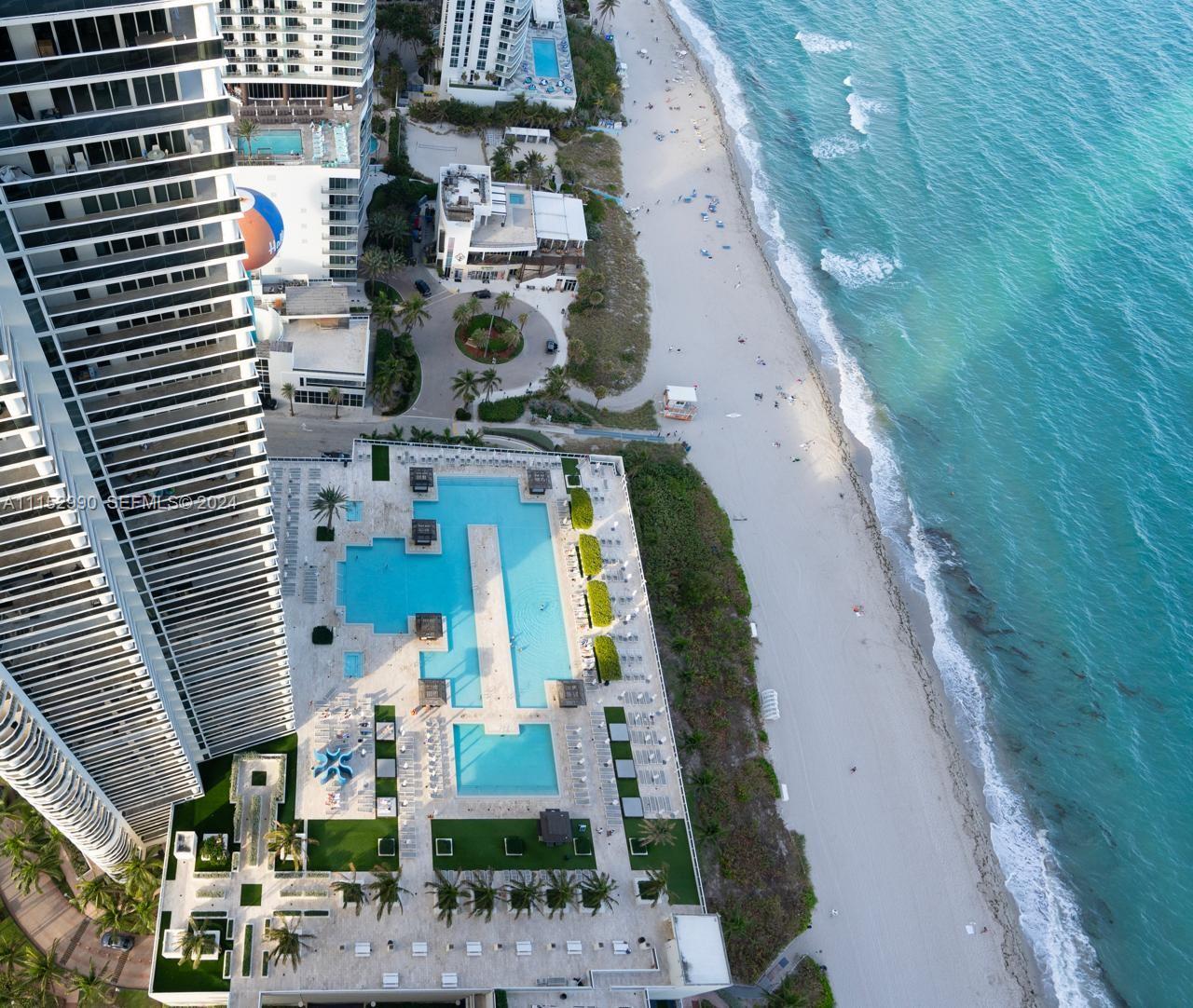 An aerial view shows a high-rise building with a large pool deck beside the beach — 1830 OCEAN DR # 4710, Hallandale Beach FL 33009, HALLANDALE BEACH, FL