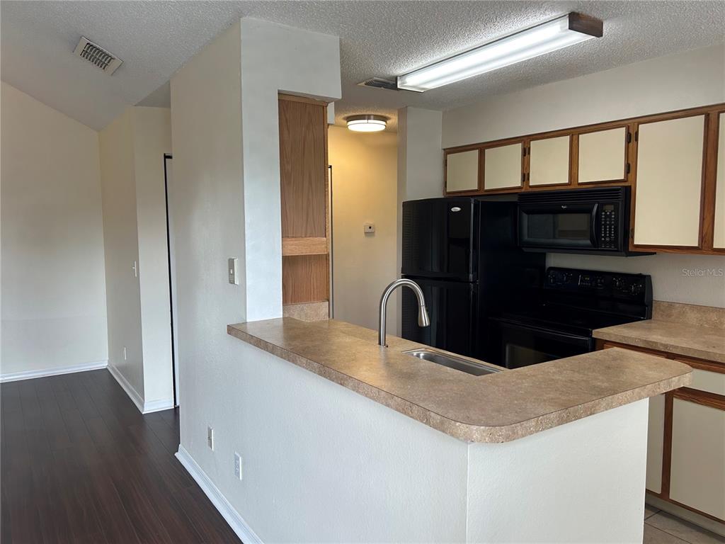 A kitchen features a breakfast bar, black appliances, and light-colored cabinets with dark trim — 1083 S HIAWASSEE ROAD UNIT 635, ORLANDO, FL