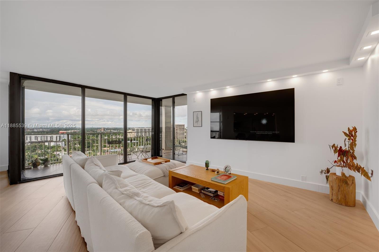 A living room features a white sofa, wooden coffee table, wall-mounted television, and balcony access — 4000 Towerside Ter # 2211, Miami FL 33138, MIAMI, FL