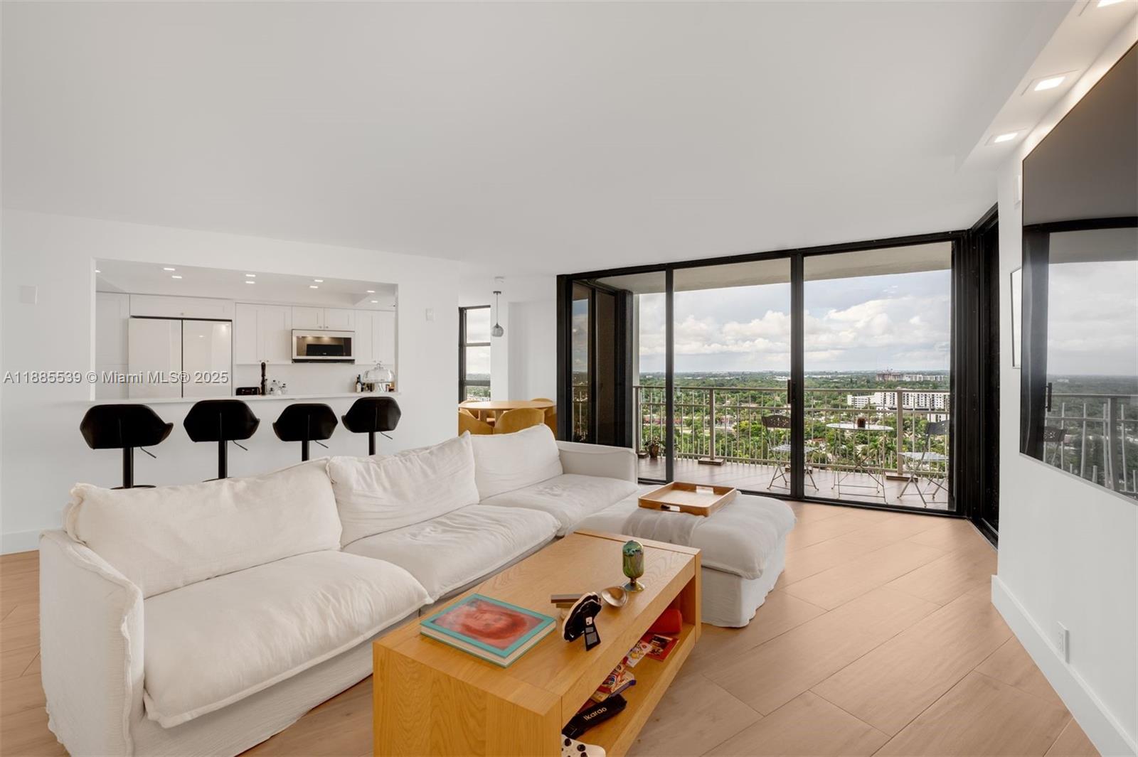 A bright living room features a white sectional sofa, wooden coffee table, and balcony access — 4000 Towerside Ter # 2211, Miami FL 33138, MIAMI, FL