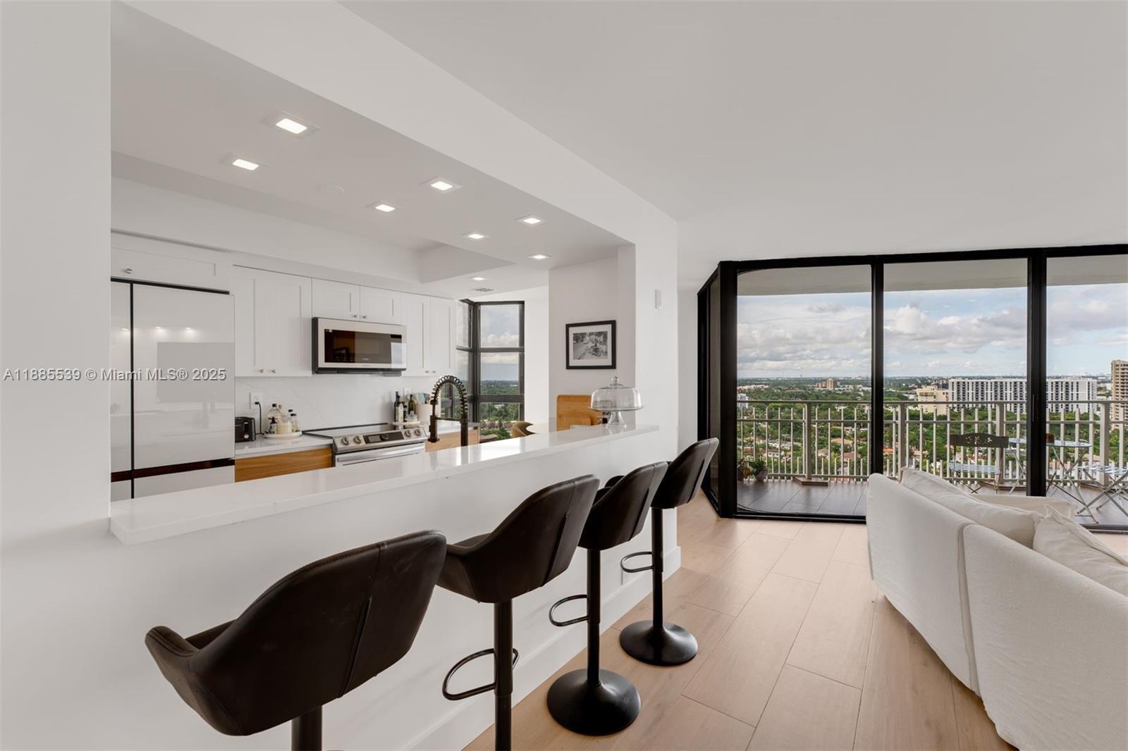 A modern kitchen with white cabinets and a breakfast bar overlooks a balcony with views — 4000 Towerside Ter # 2211, Miami FL 33138, MIAMI, FL