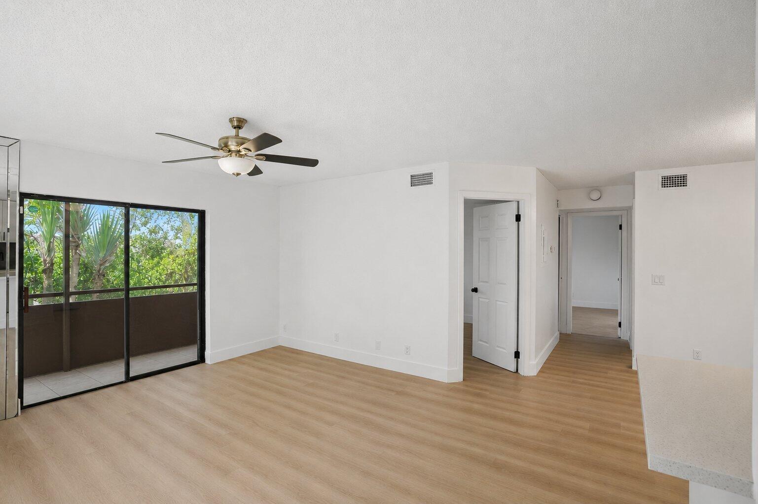 An empty living room with light wood flooring, a ceiling fan, and a sliding glass door — 588 Trace Circle # 102, Deerfield Beach FL 33441, DEERFIELD BEACH, FL